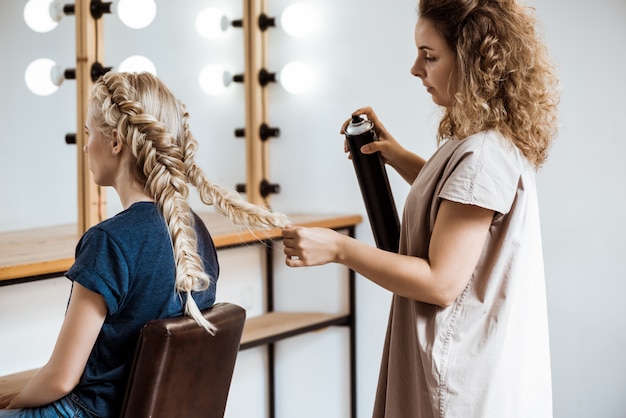 Peluquería femenina haciendo peinado a mujer rubia en salón de belleza