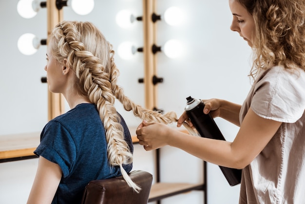 Peluquería femenina haciendo peinado a mujer rubia en salón de belleza