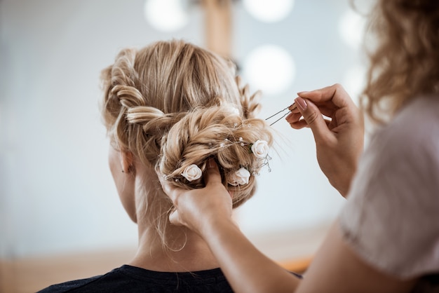 Peluquería femenina haciendo peinado a mujer rubia en salón de belleza