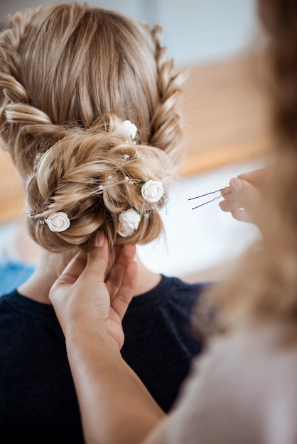 Peluquería femenina haciendo peinado a mujer rubia en salón de belleza