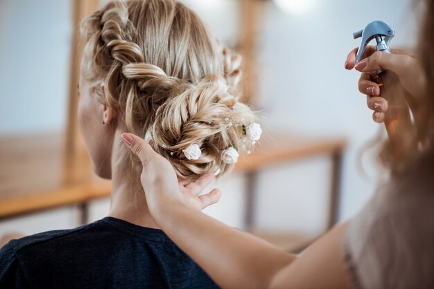 Peluquería femenina haciendo peinado a mujer rubia en salón de belleza