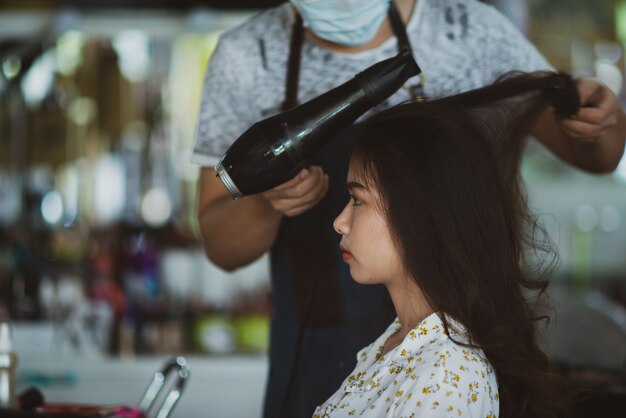 Peluquería femenina de pie, maquillaje facial y peinado a linda joven encantadora en salón de belleza