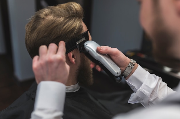 Foto gratuita peluquería irreconocible que afeita el pelo del cliente