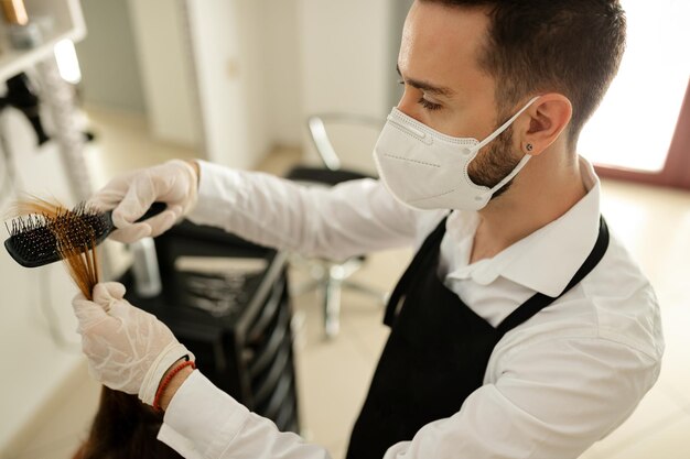 Peluquería con mascarilla protectora cepillando el cabello del cliente en un salón