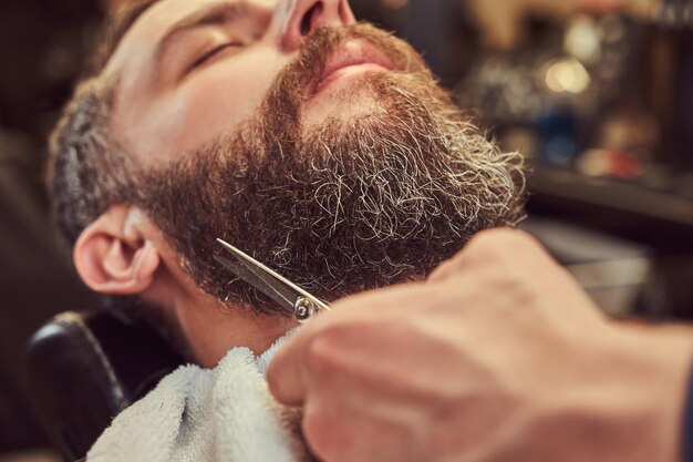 Peluquería profesional modelando barba con tijeras y peine en la barbería. Cerca de la foto.