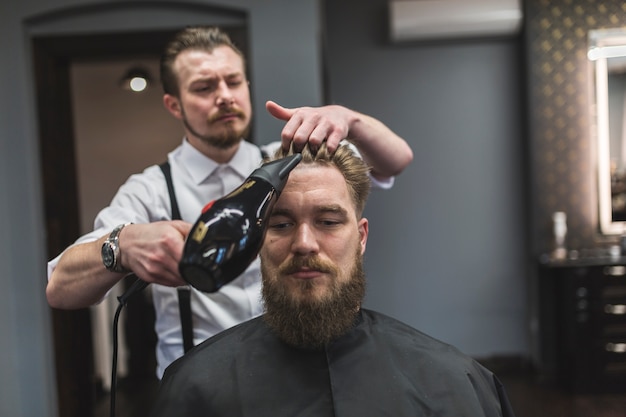 Peluquería secando el cabello del hombre barbudo