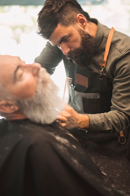 Peluquero adulto que afeita clientes barba en peluquería