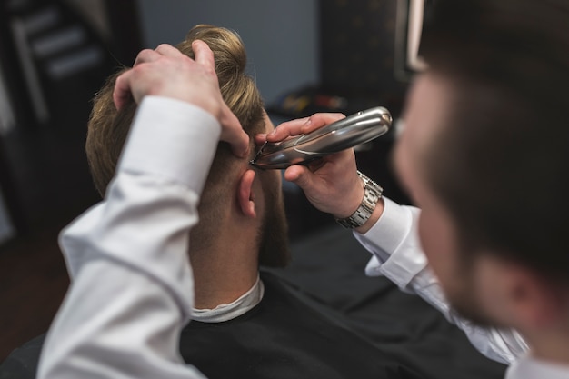 Foto gratuita peluquero sin afeitar que afeita el pelo del cliente con el condensador de ajuste