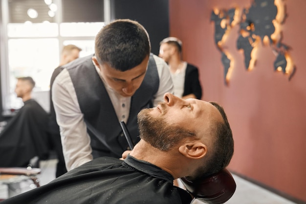 Foto gratuita peluquero calificado recortando barba de cliente masculino