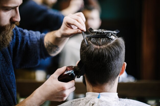 El peluquero corta el pelo del hombre con la podadora y el cepillo