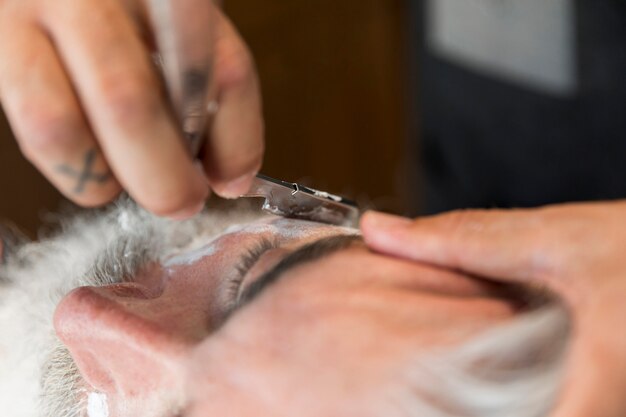 Peluquero cortando barba con navaja para cliente.