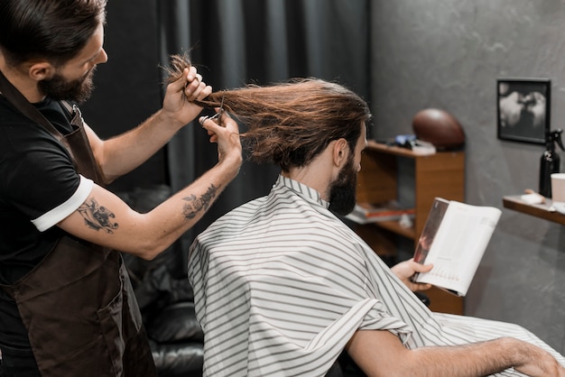 Peluquero cortando el cabello largo del hombre en peluquería