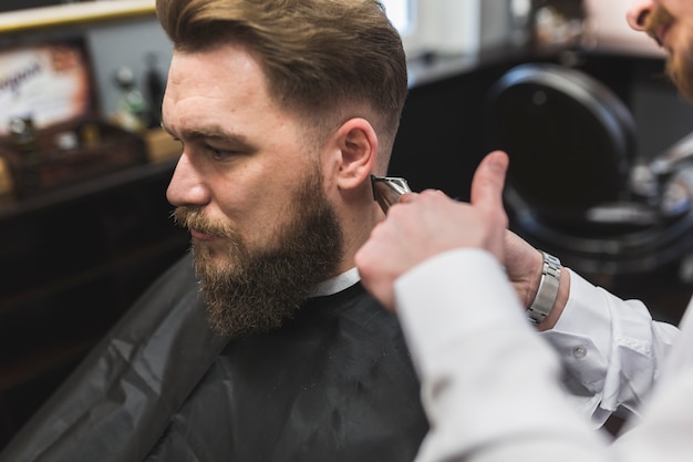 Peluquero de la cosecha que afeita el pelo del hombre barbudo