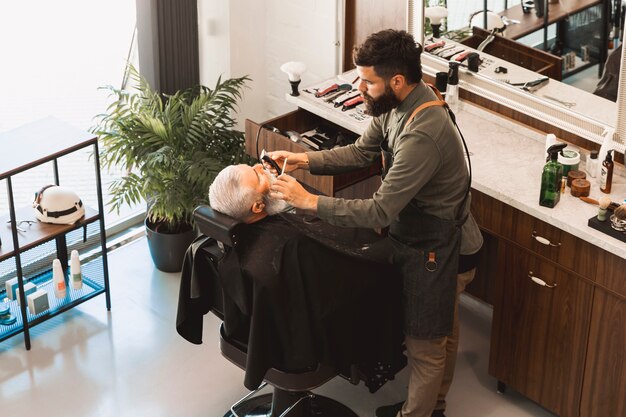 El peluquero endereza la barba con la maquinilla de afeitar y el cepillo del cliente mayor