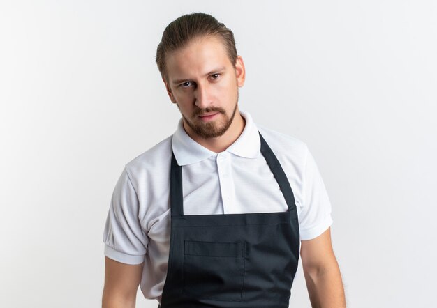 Peluquero guapo joven confiado con uniforme de pie y mirando aislado en blanco con espacio de copia