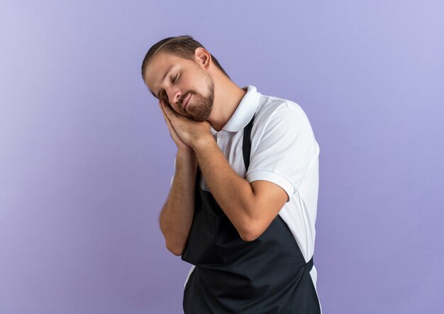 Peluquero guapo joven soñador vistiendo uniforme haciendo gesto de sueño con los ojos cerrados aislados en púrpura con espacio de copia