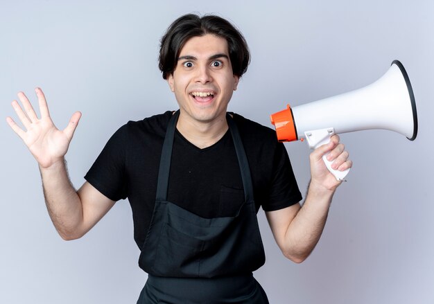 Peluquero masculino hermoso joven alegre en uniforme que sostiene el altavoz y la mano extendida aislada en el fondo blanco