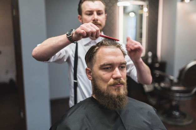 Peluquero peinando el cabello del hombre antes de cortar