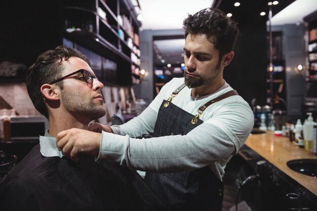 Peluquero poniendo capa sobre el cuello de los clientes