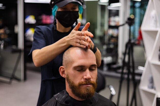 Peluquero profesional con mascarilla protectora, corte de pelo para hombre brutal barbudo europeo en salón de belleza