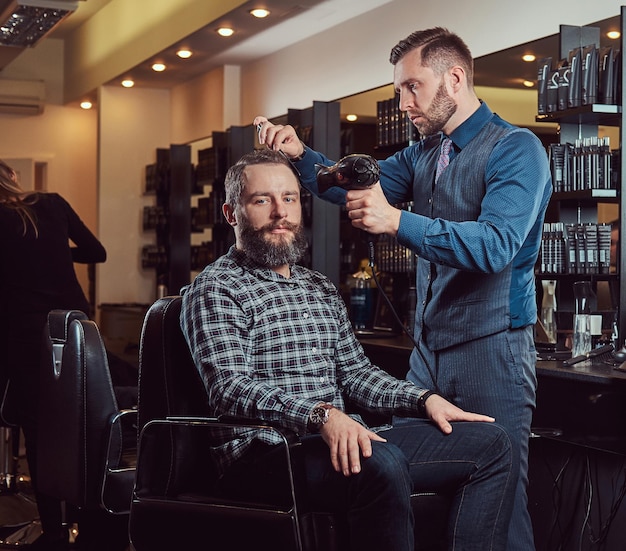 Peluquero profesional que trabaja con un cliente en un salón de peluquería, utiliza un secador de pelo. Corte de pelo de hombres en una barbería.