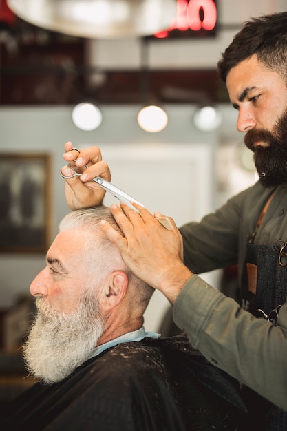 Peluquero profesional con tijeras para peinar el cabello del anciano.