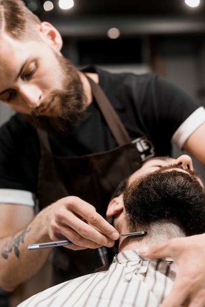 Peluquero que afeita la barba del cliente con la maquinilla de afeitar