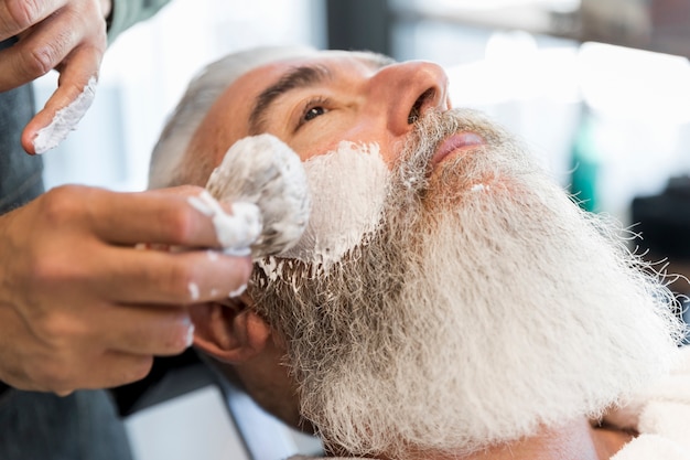 Peluquero que se prepara para afeitar al cliente mayor