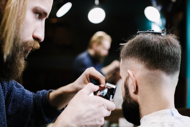 El peluquero quita el pelo del hombre con una podadora