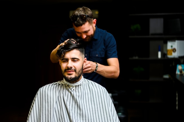 Peluquero de tiro medio cortando el cabello del cliente