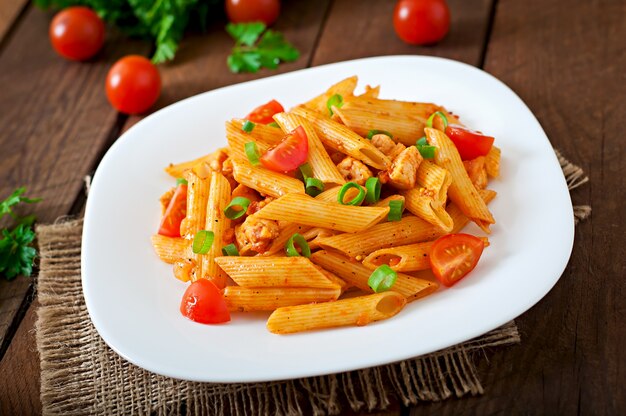 Penne pasta en salsa de tomate con pollo y tomates en una mesa de madera