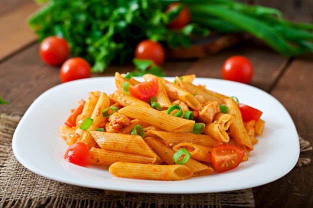 Penne pasta en salsa de tomate con pollo y tomates en una mesa de madera