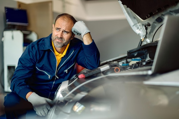 Foto gratuita pensamiento mecánico adulto medio mientras repara el motor de un automóvil en un taller