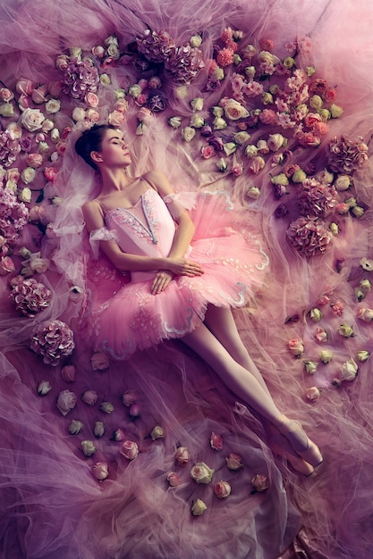 Pensando en calentar. Vista superior de la hermosa joven en tutú de ballet rosa rodeada de flores. Ambiente primaveral y ternura a la luz coralina. Foto de arte. Concepto de primavera, flor y despertar de la naturaleza.