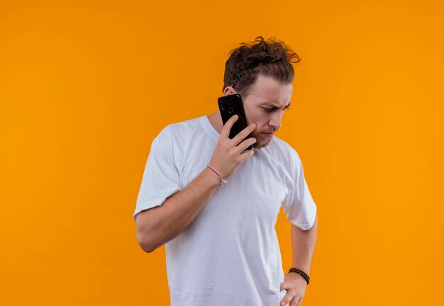 Pensando en chico joven con camiseta blanca habla en el teléfono en la pared naranja aislada