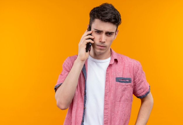 Pensando en el chico joven caucásico con camisa rosa habla por teléfono en la pared naranja aislada