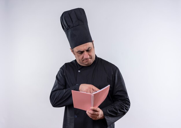 Pensando en el cocinero masculino de mediana edad en uniforme de chef leyendo algo en el cuaderno en su mano