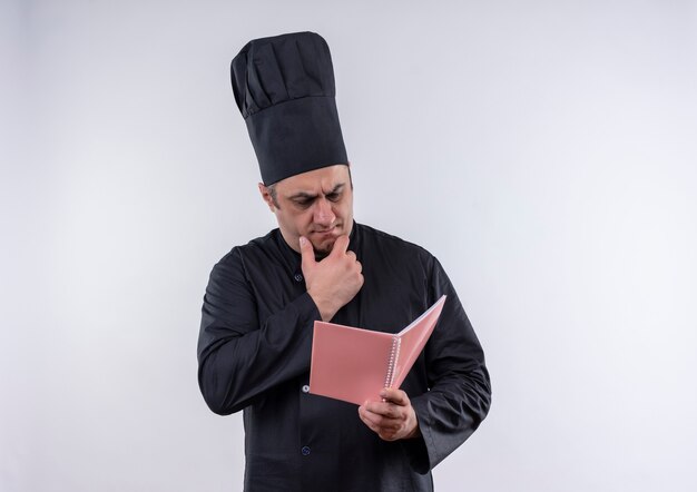 Pensando cocinero masculino de mediana edad en uniforme de chef mirando portátil en su mano