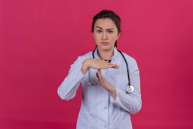 Foto gratuita pensando doctor joven vistiendo bata médica y estetoscopio mostrando gesto de tiempo de espera sobre fondo rojo isoleted