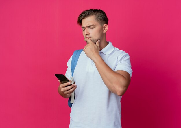 Pensando joven apuesto estudiante masculino con bolsa trasera sosteniendo