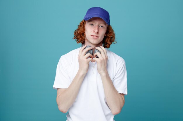 Pensando en un joven apuesto con gorra usando audífonos aislados de fondo azul