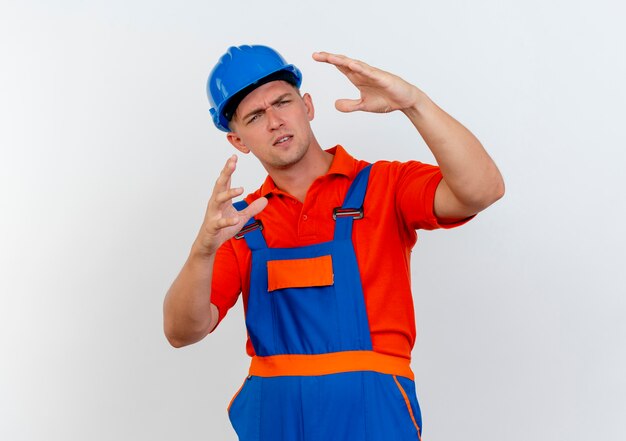 Foto gratuita pensando en el joven constructor con uniforme y casco de seguridad que muestra el tamaño en blanco