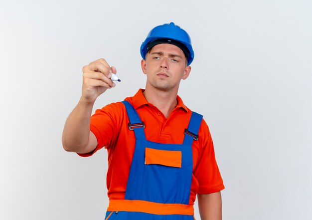 Pensando en el joven constructor con uniforme y casco de seguridad sosteniendo y mirando el marcador en blanco