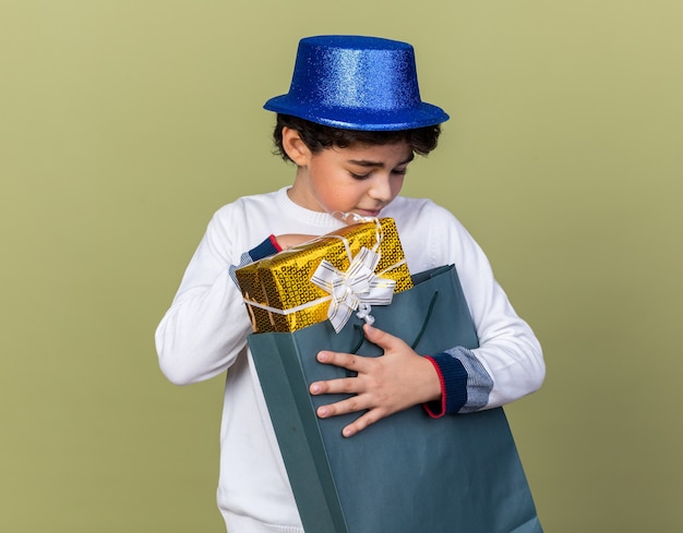 Pensando en el niño pequeño con sombrero de fiesta azul sosteniendo y mirando la bolsa de regalo