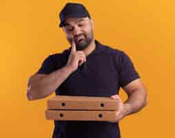 Foto gratuita pensando en el repartidor de mediana edad en uniforme y gorra sosteniendo y mirando cajas de pizza poniendo el dedo en la mejilla aislada en la pared amarilla