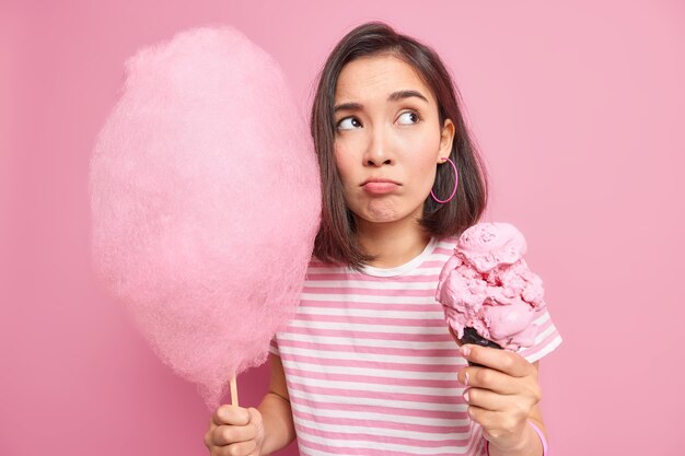 Pensativa mujer de cabello oscuro mira hacia otro lado con tristeza sostiene un delicioso helado de cono grande de algodón de azúcar. Disparo monocromo