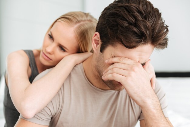 Pensativa mujer infeliz consuela a su hombre triste mientras están sentados en la cama