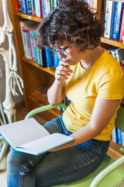 Pensativa mujer sentada y leyendo el libro en la biblioteca