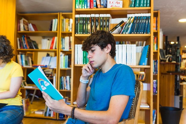 Pensativo adolescente leyendo en la biblioteca