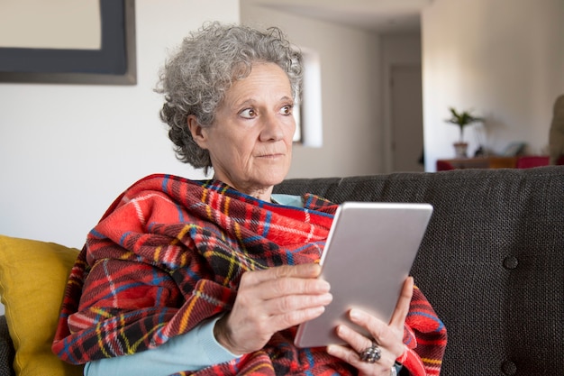 Foto gratuita pensativo frunciendo el ceño senior mujer leyendo un libro en línea en la tableta